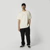 Mann im cremefarbenen oversized T-Shirt mit Kappe und schwarzer Hose