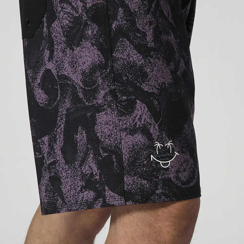 Detailaufnahme Smiley-Logo mit Palmen auf texturiertem schwarz-lila Boardshort-Stoff